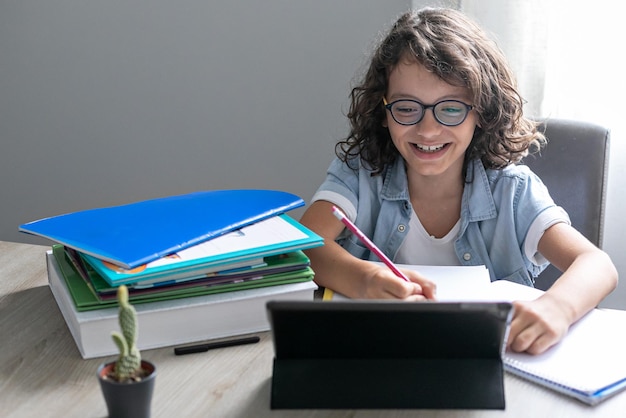 Little adorable school boy with eyeglasses studying online from home kid using digital tablet