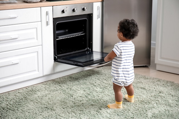 Little African-American baby near stove in kitchen. Child in danger