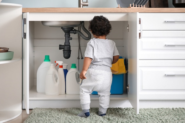 Little African-American baby playing with detergents at home. Child in danger