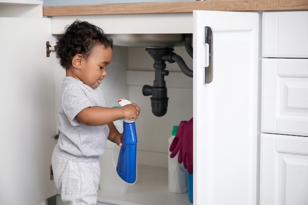 Little African-American baby playing with detergents at home. Child in danger