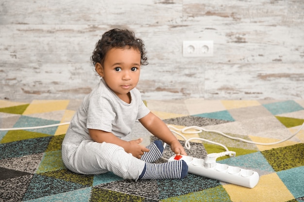 Little African-American baby playing with extension cord at home. Child in danger