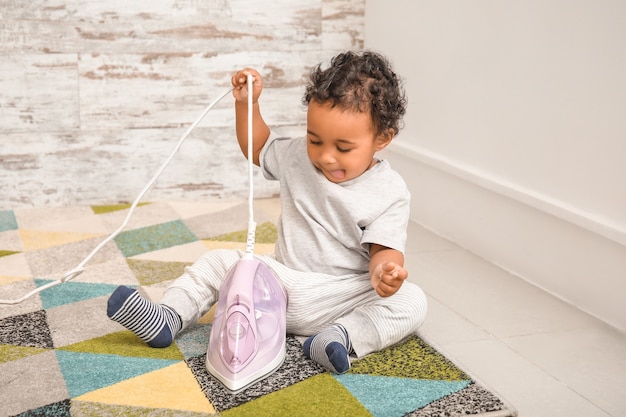 Little African-American baby playing with iron at home. Child in danger