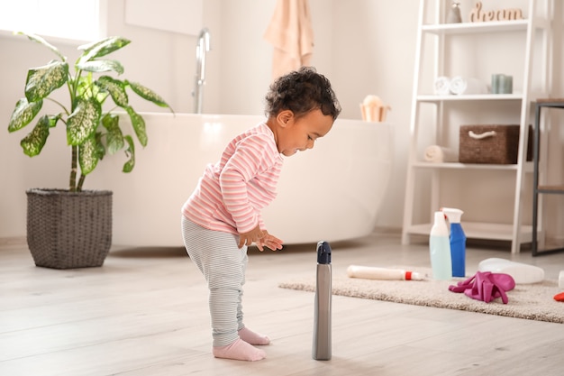 Little African-American baby playing with washing liquids at home. Child in danger