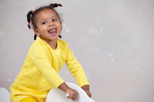 Little African American girl in yellow clothes shows tongue Funny child