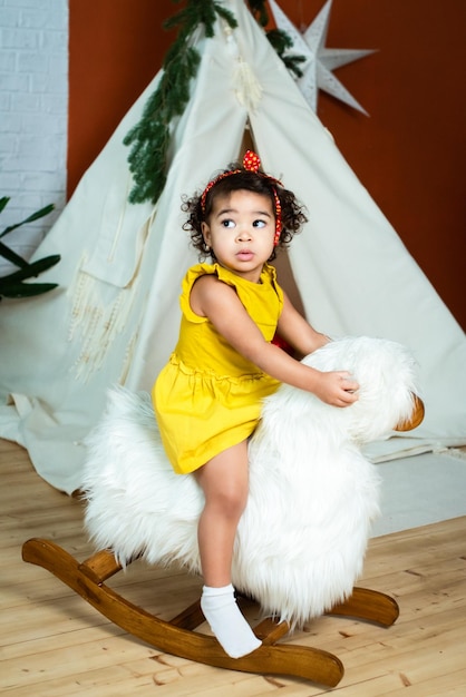 Little african black girl is rocking on a rockinghorse baby with dark skin color afraid