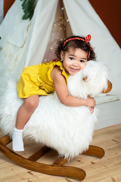 Little african black girl is rocking on a rockinghorse sheep baby with dark skin color smiling