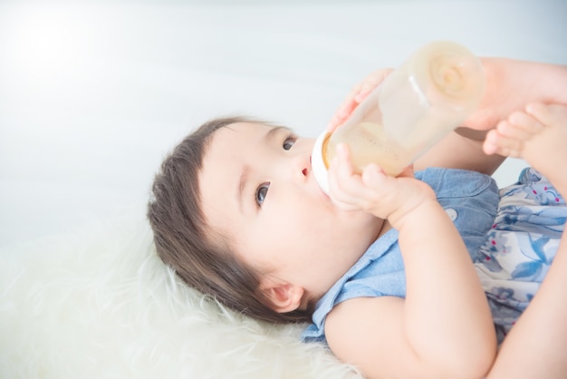 Little asian baby girl drinking milk from bottle by herself on bed