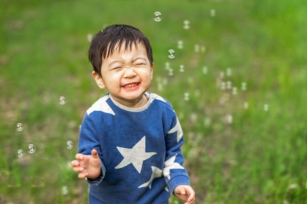 Little Asian boy happily playing with soap bubbles with happy face in summer