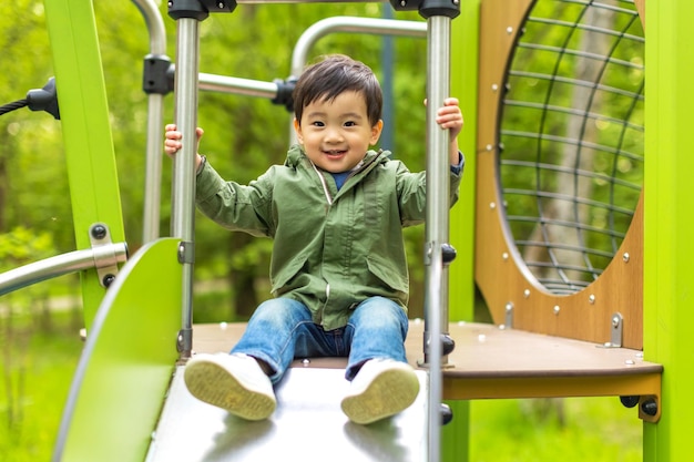 Little Asian boy is playing on the wooden playground with happy face in summer outdoors and looking at the camera with a smile