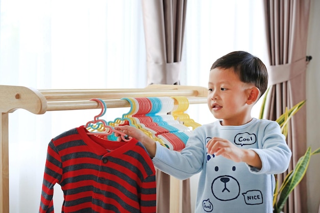 Little Asian boy using hanger hang up a clothes on wood rack