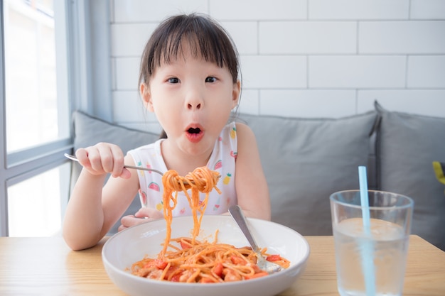 Little asian girl enjoy eating spaghetti on table at restaurant