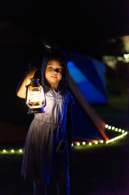 Little asian girl holding a vintage lantern while camping in dark night