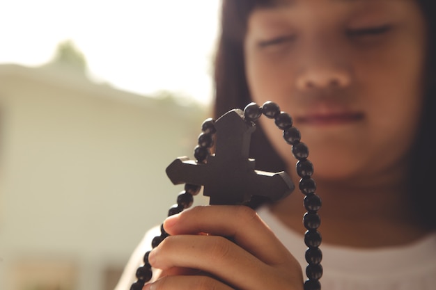 Little Asian girl praying with holding the cross, Christian concept.