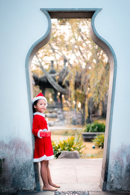 Little asian girl in red Santa Claus costume with present box in the door