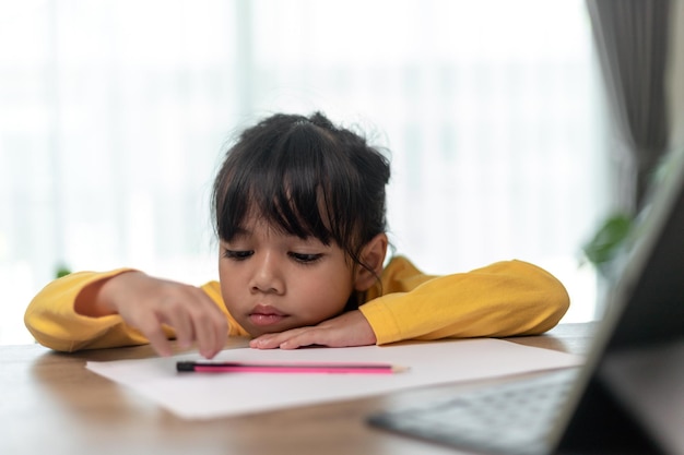 Little Asian girl sitting alone and looking out with a bored face Preschool child laying head down on the table with sad bored with homework spoiled child