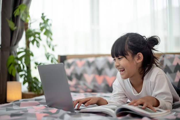 Little Asian girl using a laptop while lying on the bed