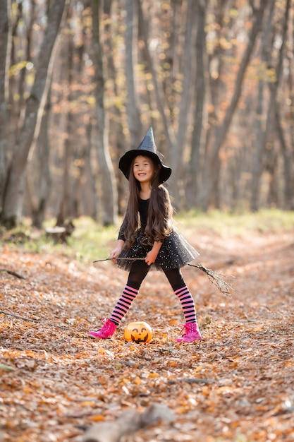 A little Asian girl in a witch costume for Halloween walks in the forest with a bucket for sweets