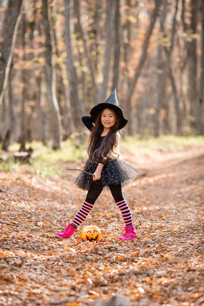 A little Asian girl in a witch costume for Halloween walks in the forest with a bucket for sweets