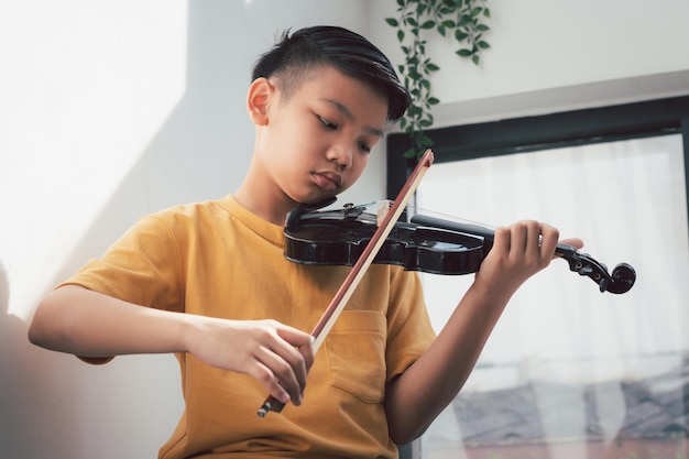 A Little Asian kid playing and practice violin musical string instrument against in home