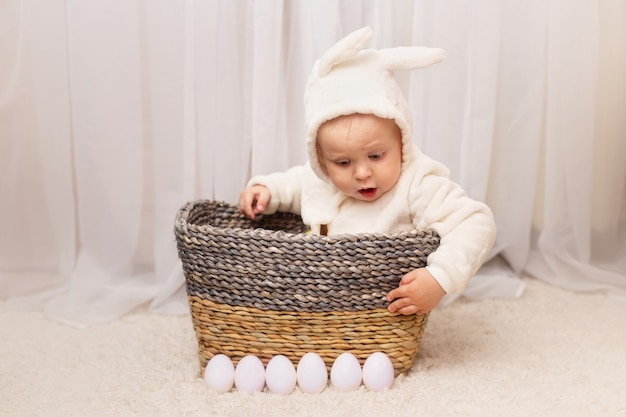 Little baby in bunny costume sitting in the basket with easter eggs at home