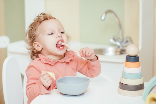 Little baby eats pasta in the children's kitchen