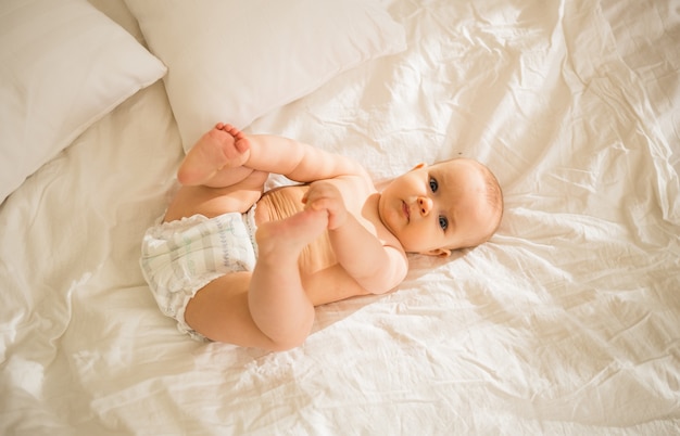 A little baby girl in a diaper lies on the bed a