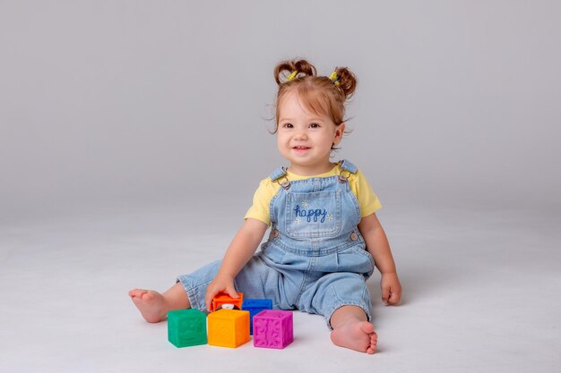 little baby girl is sitting on a white background and playing with colorful cubes. kid's play toy