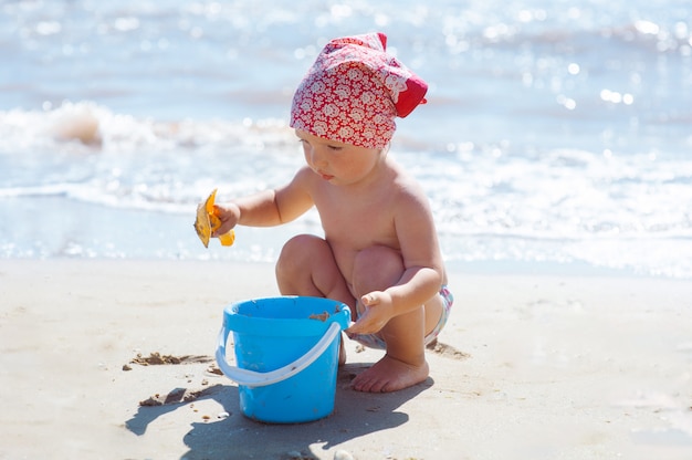 Little baby girl plays with sand and build castle on beach