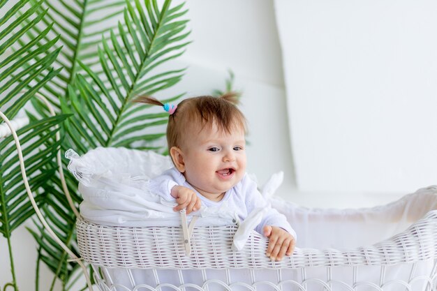 Little baby girl sits in a white stroller at home with a sly look