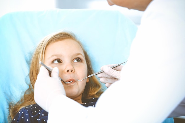 Little baby girl sitting at dental chair with open mouth during oral check up while doctor. Visiting dentist office. Medicine concept. Toned photo.