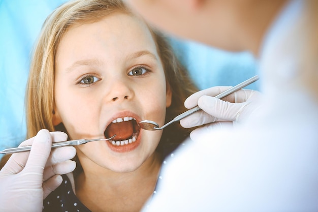 Little baby girl sitting at dental chair with open mouth during oral check up while doctor. Visiting dentist office. Medicine concept. Toned photo.