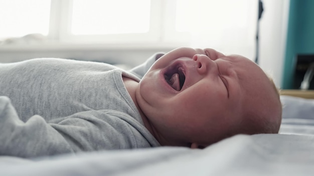 Little baby in grey bodysuit screams out loud calling mother