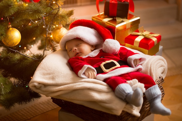 Little baby Santa sleeping under Christmas tree with presents