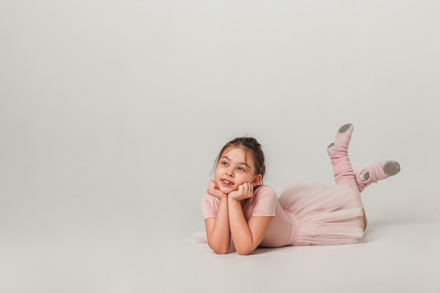 Little ballerina dancer in a pink tutu academy student posing on white background