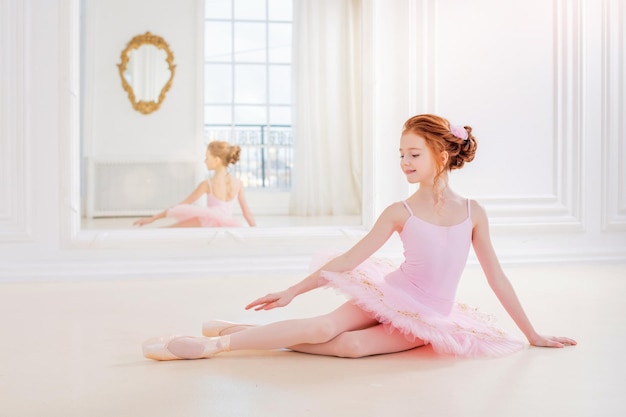 Little ballerina girl in a pink tutu and pointe shoes posing in a white studio