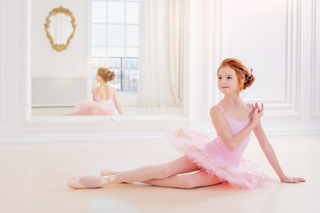 Little ballerina girl in a pink tutu and pointe shoes posing in a white studio