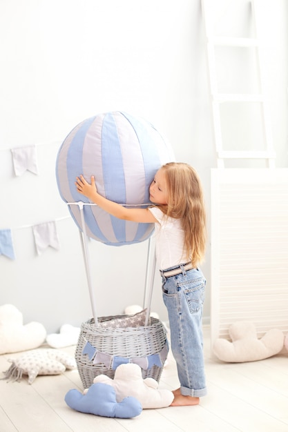 Little beautiful girl in casual clothes stands on a decorative balloon. The child plays in the children room. The concept of childhood, travel. birthday, holiday decorations interior