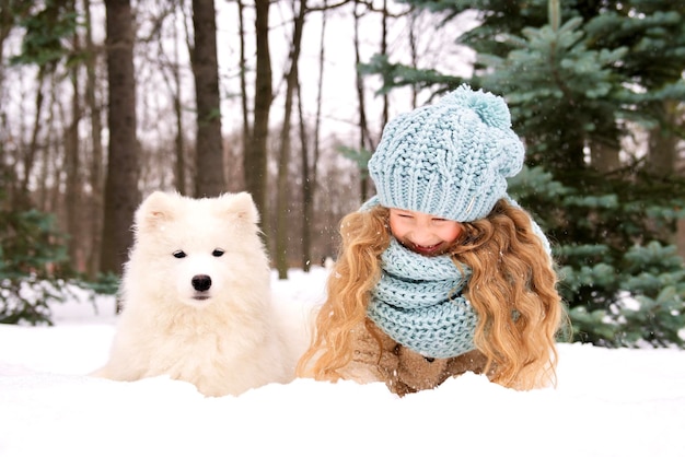 Little beautiful girl, cute happy positive child kid in snow having fun with her dog at winter