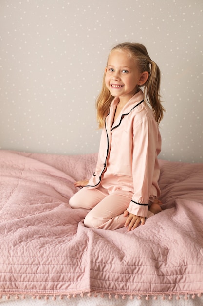 little beautiful girl in pink pajamas sits on a pink blanket on the bed at home