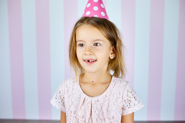 Little beautiful girl wearing birthday pink cap on pink white stripe background