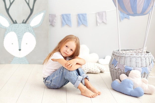 Little beautiful girl in a white T-shirt and jeans sits on the wall of a decorative balloon. The child plays in the children's room. The concept of childhood, travel. birthday holiday decoration