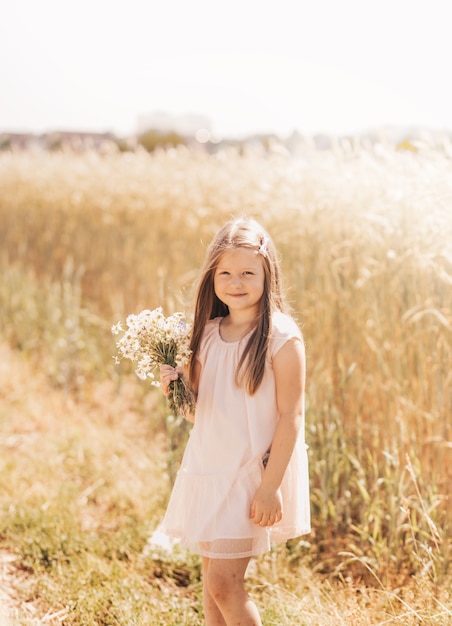 A little beautiful girl with a bouquet of daisies in a wheat field