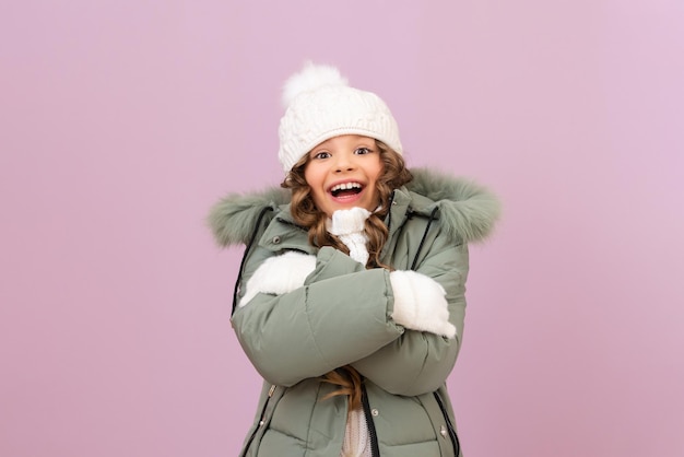 A little beautiful girl with curly hair in a warm knitted hat and jacket is very happy about winter. baby clothes for a girl for the winter season.