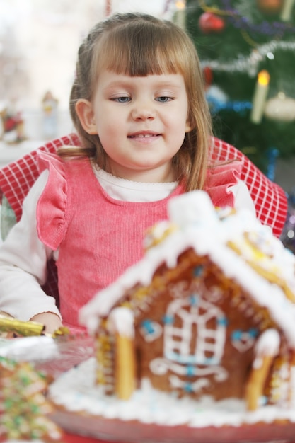 Little beautiful girl with a house of gingerbread dough