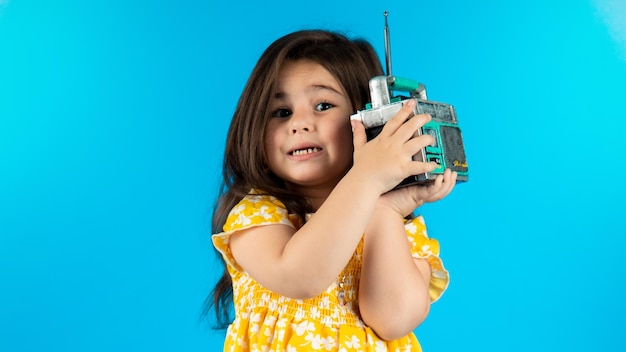 Little beautiful smiling girl with a funny face in a striped yellow dress posing on a blue background in studio