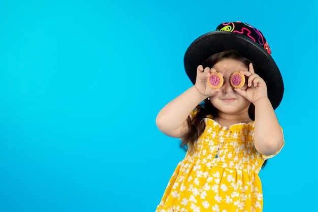 Little beautiful smiling girl with a funny face in a striped yellow dress posing on a blue background in studio