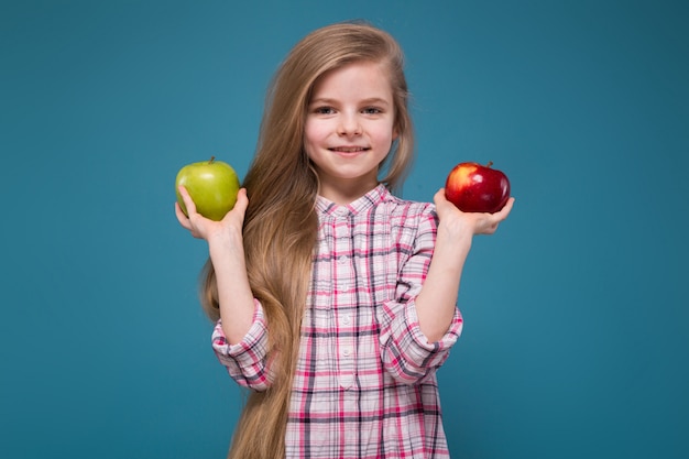 Little beauty girl in shirt with long brown hair with apple in hands