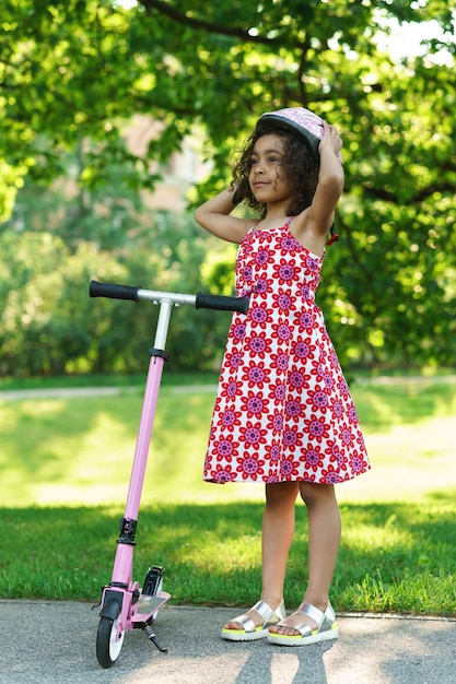 Little black girl with a kick scooter in a city park