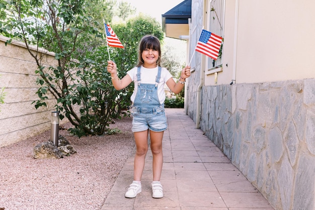 Little blackhaired girl with American flags in the garden of her house Concept of celebration independence day 4th of July patriotism holiday and American pride