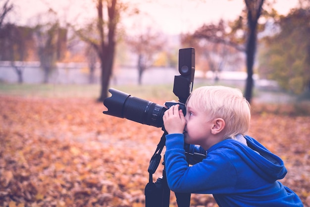 Little blond boy shoots with a large SLR camera on a tripod Photo session in the autumn park